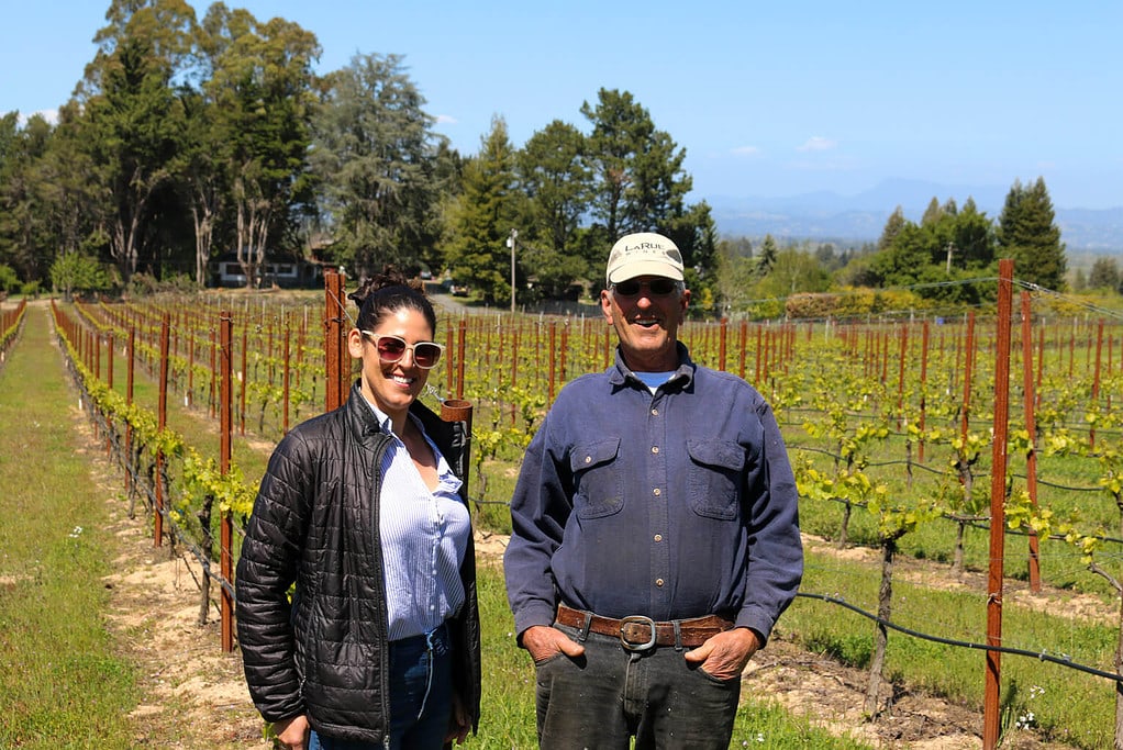 Ten Klopp and Lauren Klopp Williams centred in the foreground, with H Klopp VIneyard in the mid-ground, rows of vines extending to the background. 