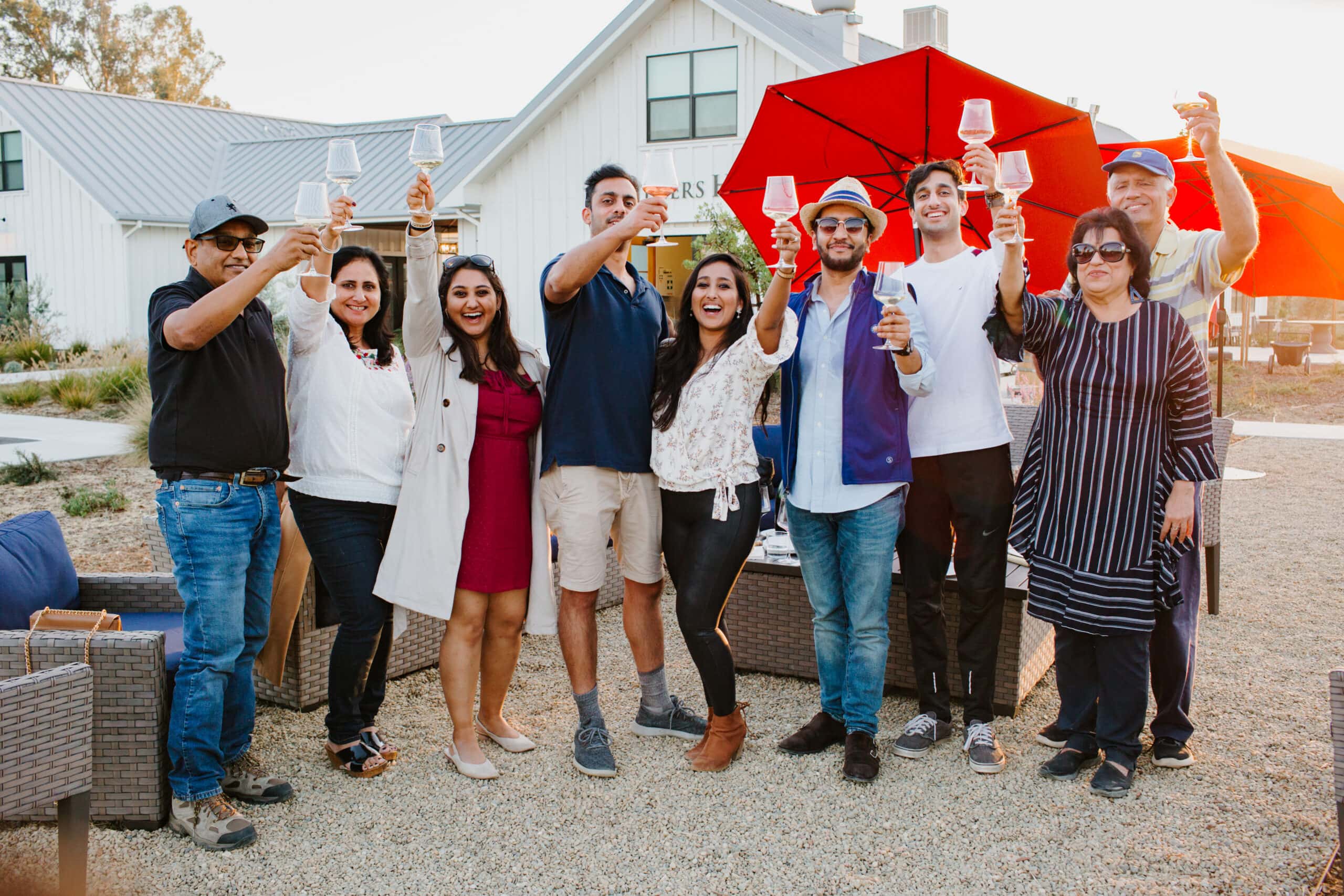 A group of people are standing in front of the Vitners House for a group photo while raising their wine glasses.