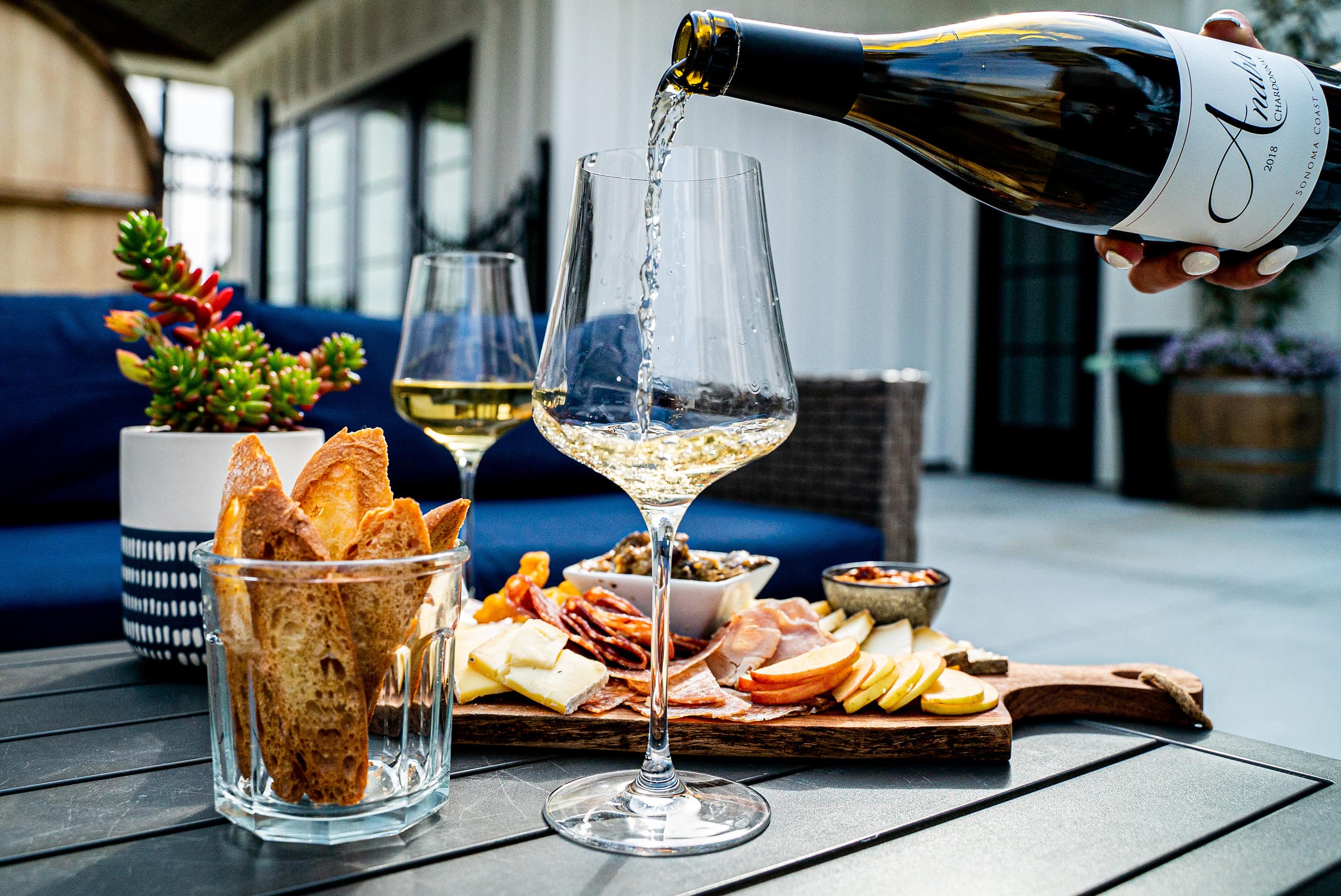 A glass of Anaba Sonoma Coast Chardonnay being poured next to a cheese board.