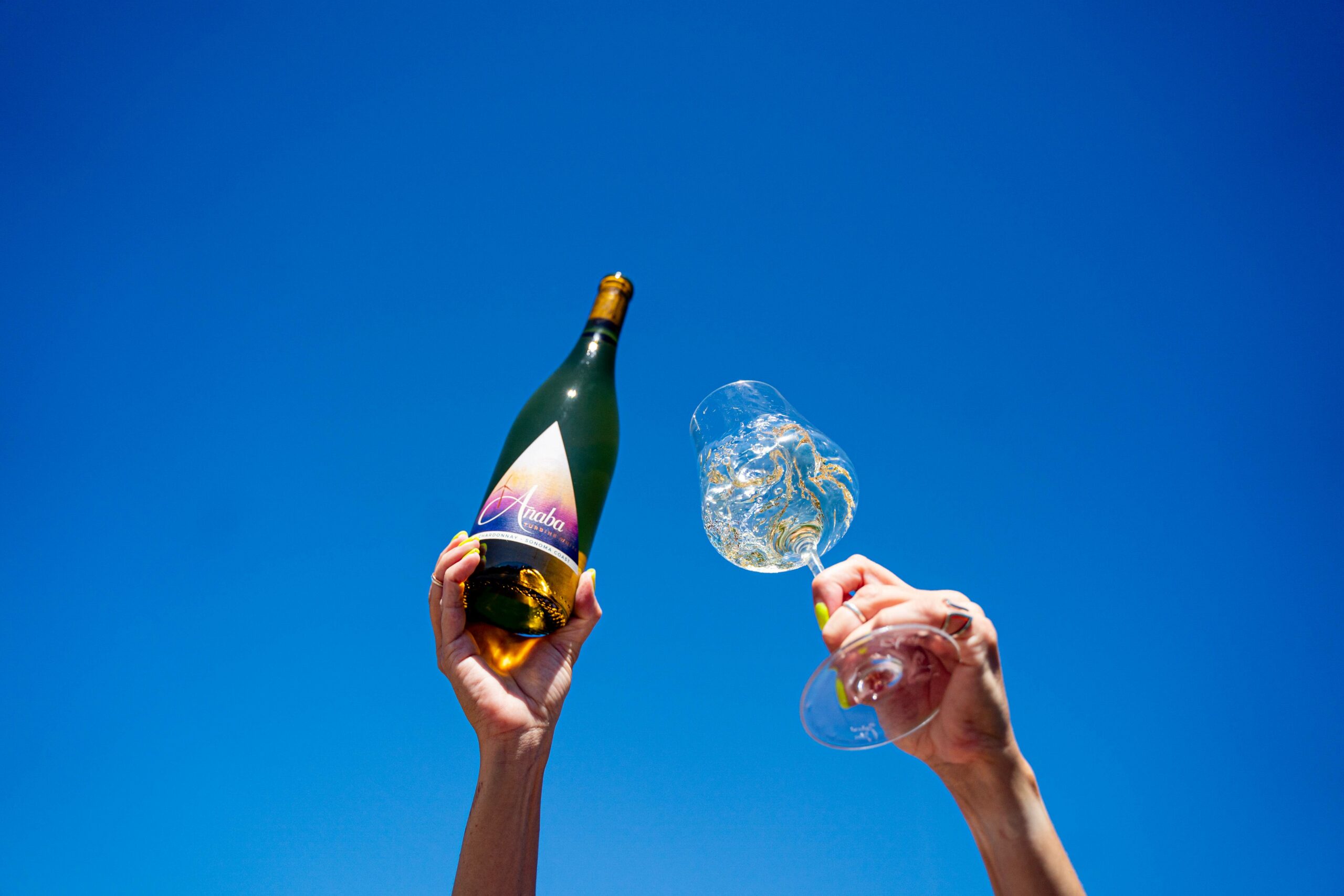 Woman holding bottle of Anaba Turbine White Wine and glass of white wine, set against a clear blue sky.