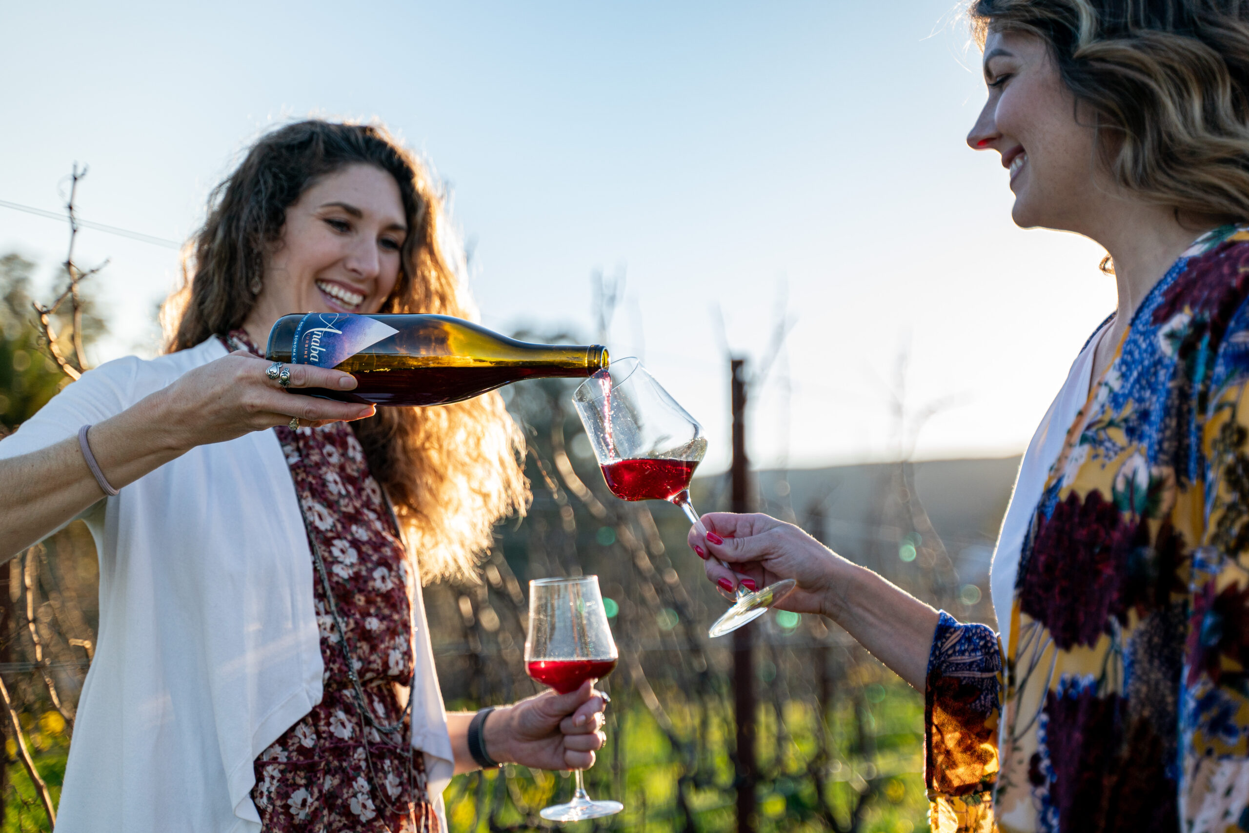 Rose and Emily pouring wine in the vineyard.