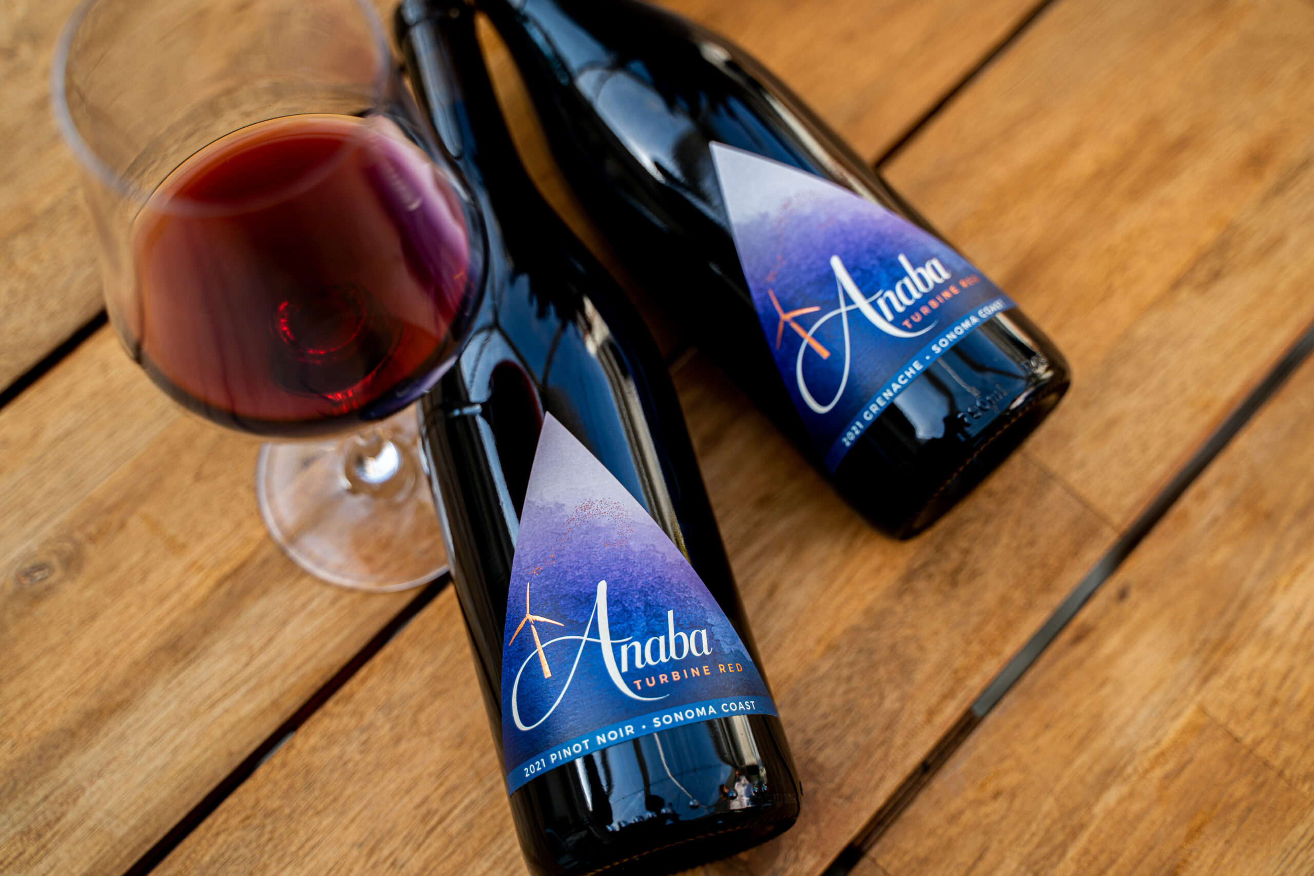 Turbine Grenache and Pinot Noir bottles with a glass of red on a table.