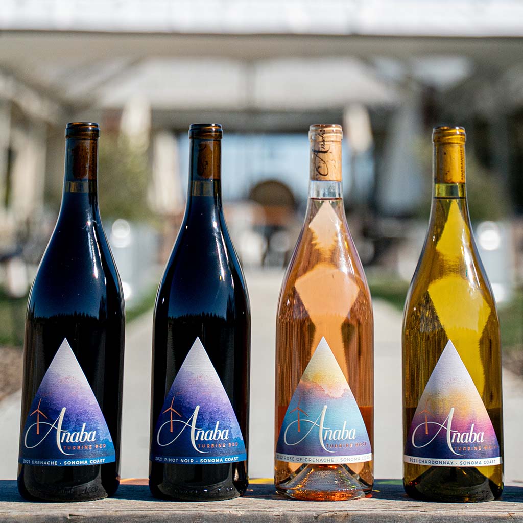 Four Anaba wine bottles placed on a table in the foreground, the vineyard courtyard blurred in the background. 