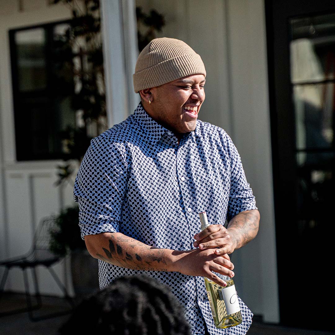 A young man holding a bottle of Anaba white wine, laughing joyously to others out of frame. 