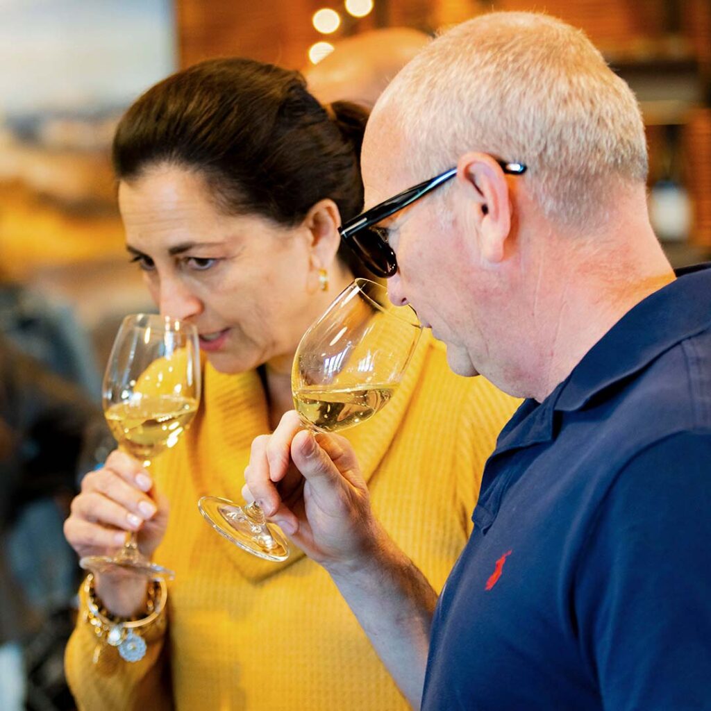 A man and a woman raising two glasses of Anaba white wine to their noses. 