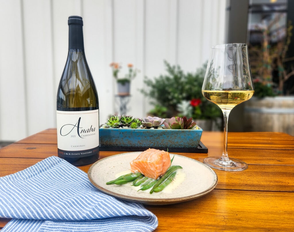 Glass and bottle of white wine on wood table with plate of salmon and cream sauce
