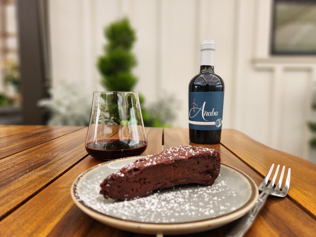slice of chocolate cake on plate on wood table with glass of wine and bottle of Anaba port