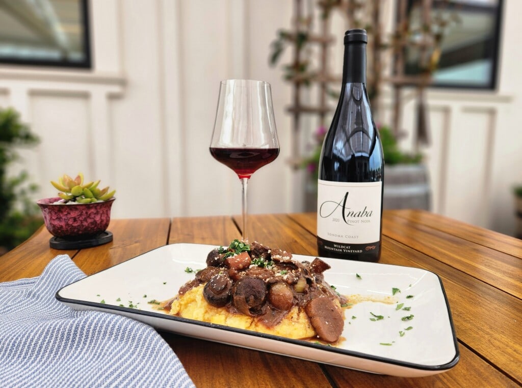 Plate of polenta and mushroom bourginon on wood table with bottle and glass of red wine
