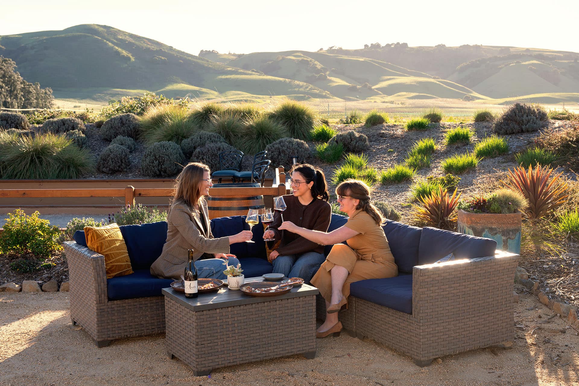 Three women sitting on a couch in the Anaba courtyard, with green hills of Sonoma in the background.